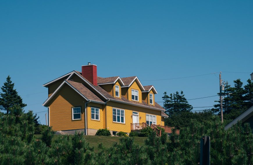 A vibrant yellow house nestled in the countryside of Percé, QC, Canada, surrounded by lush greenery.